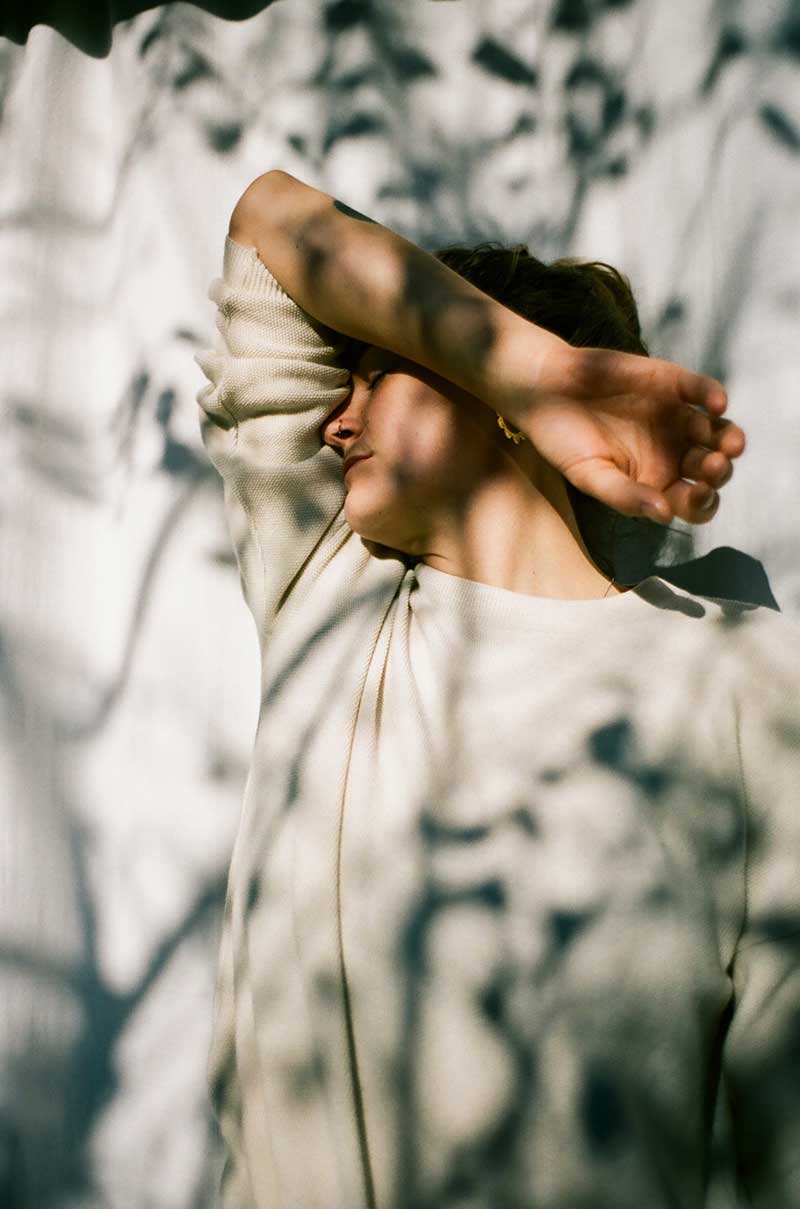Person mit Gesicht in Ellbogen überdeckt von Schatten aus Pflanzen