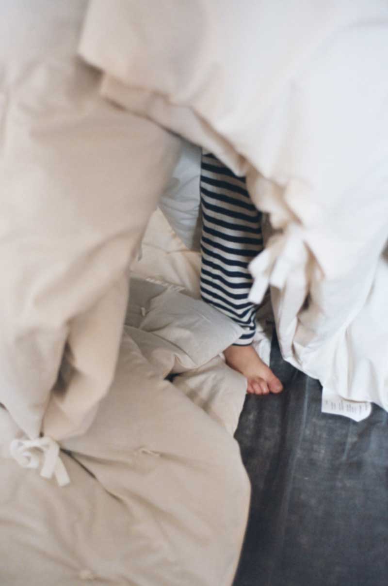 Kinderfüsse in Pyjama verstecken sich unter Bettdecke.