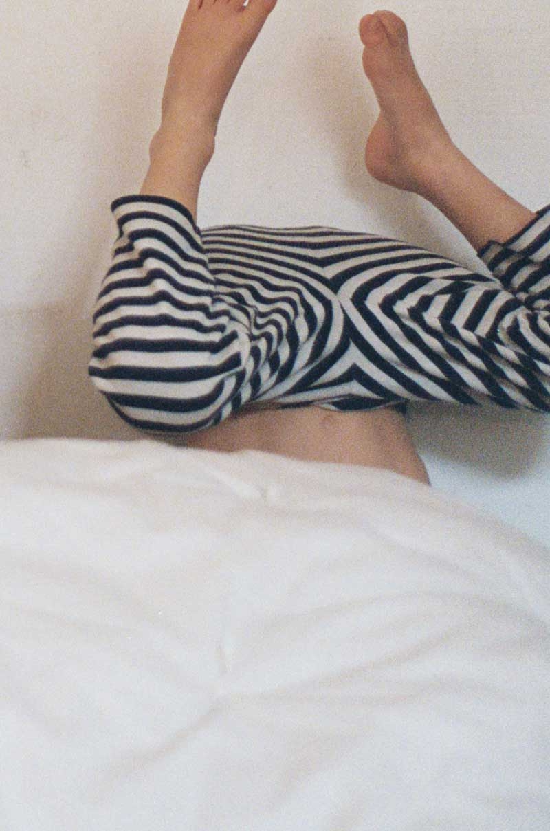 Kinderbeine in gestreiften Pyjama gucken im Kopfstand aus Decke hervor.